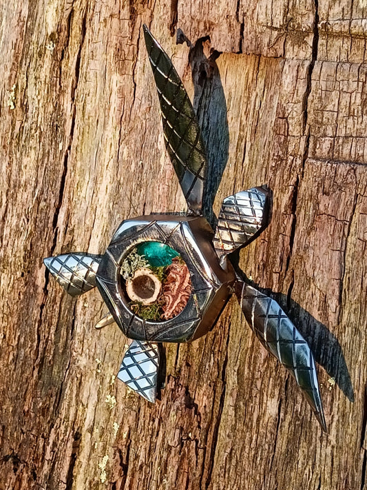 small metal turtle made from a nut taken from a brewery and filled with organics and glass beads.