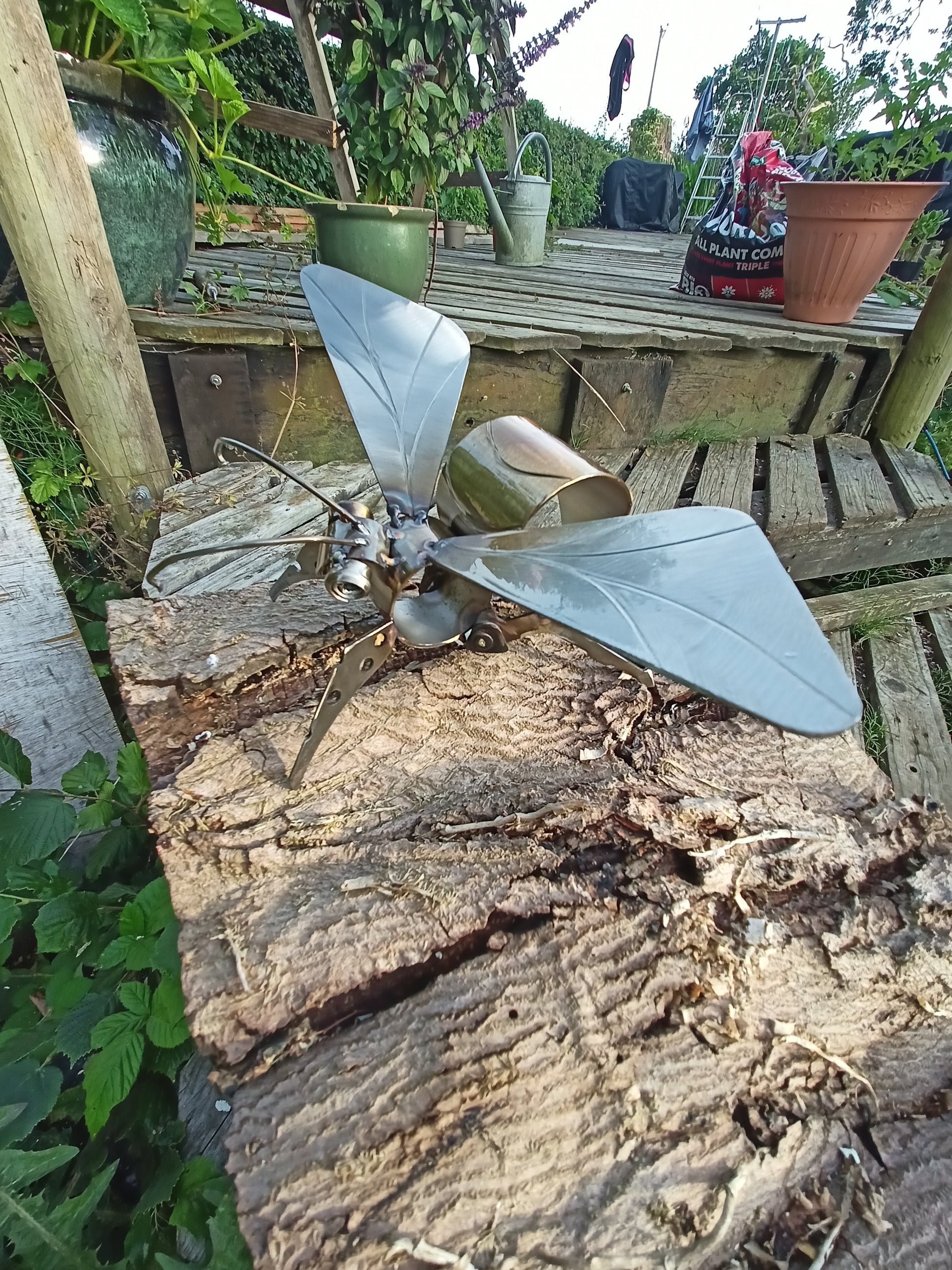 A lacquered stainless steel bee artwork placed outdoors, clinging to wood