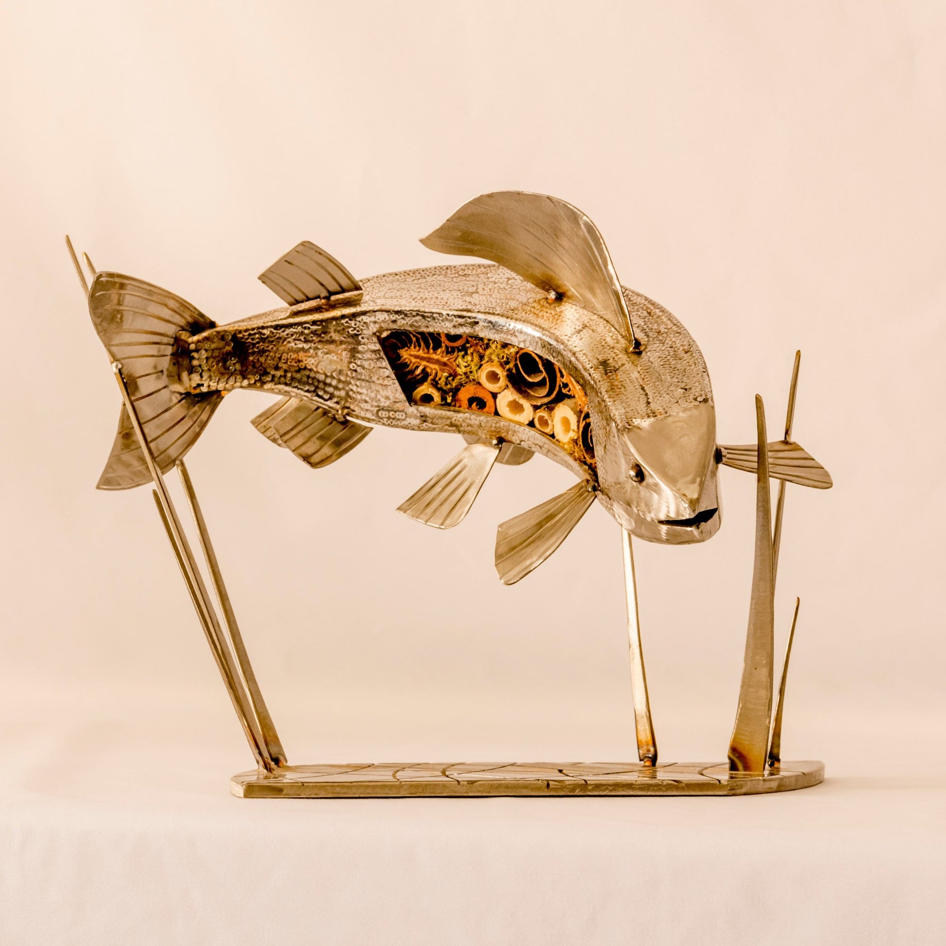 A silver sculpture of a grayling fish with applied scales, mounted on a stand.