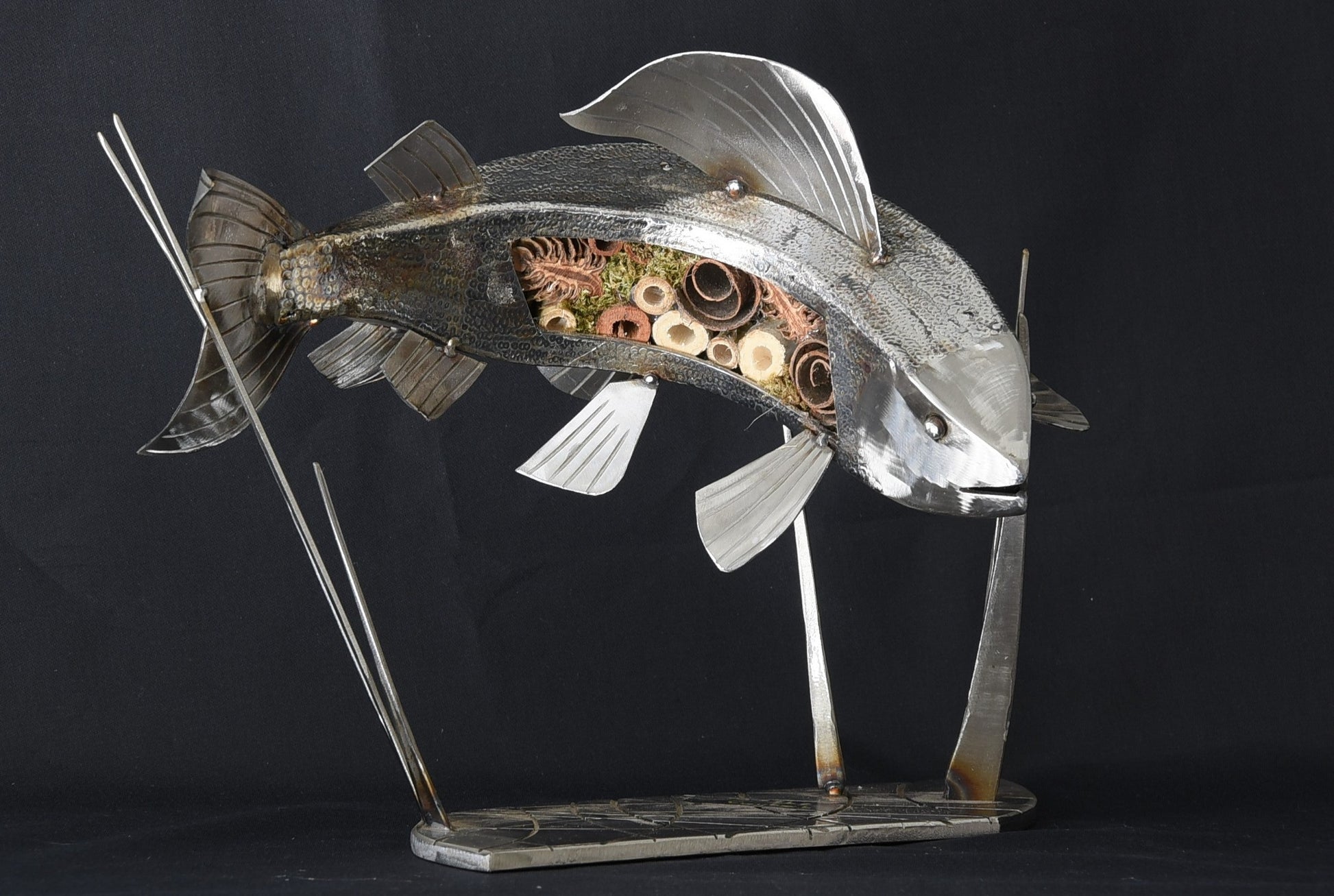 A silver sculpture of a grayling fish with applied scales, mounted on a stand.