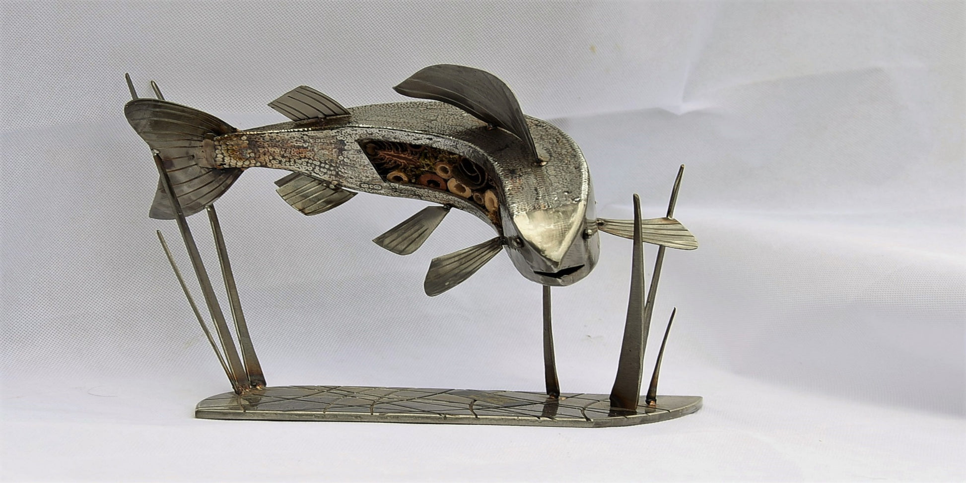 A silver sculpture of a grayling fish with applied scales, mounted on a stand.