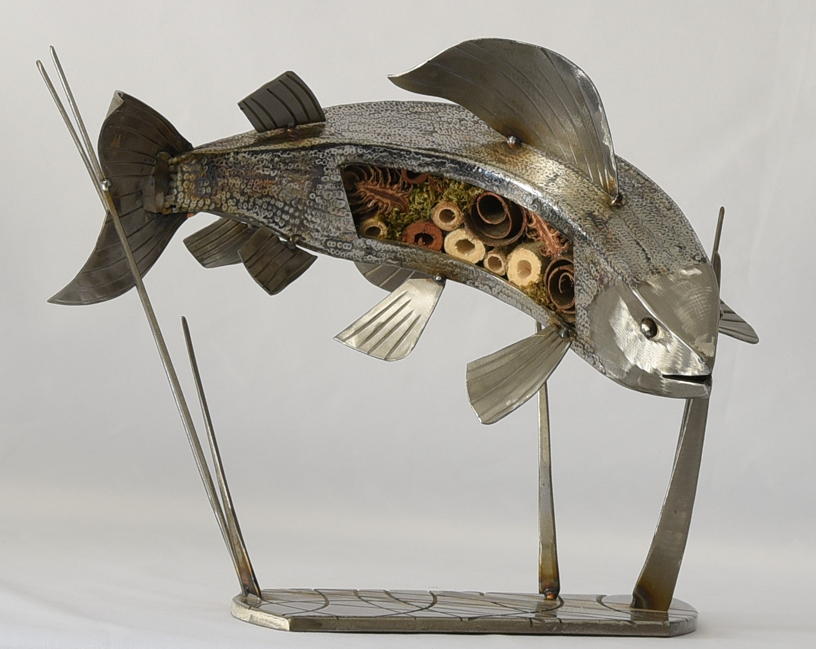 A silver sculpture of a grayling fish with applied scales, mounted on a stand.
